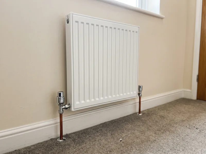 A newly fitted white radiator with chrome valves and tidy pipework